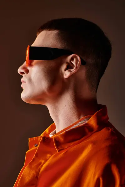Side view image of stylish man in orange shirt and sunglasses on brown background — Stock Photo