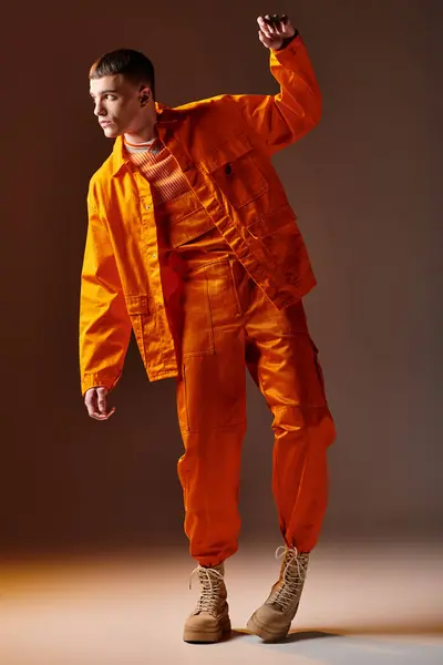 Tiro de comprimento total de homem elegante em macacão laranja e casaco posando no fundo marrom — Fotografia de Stock