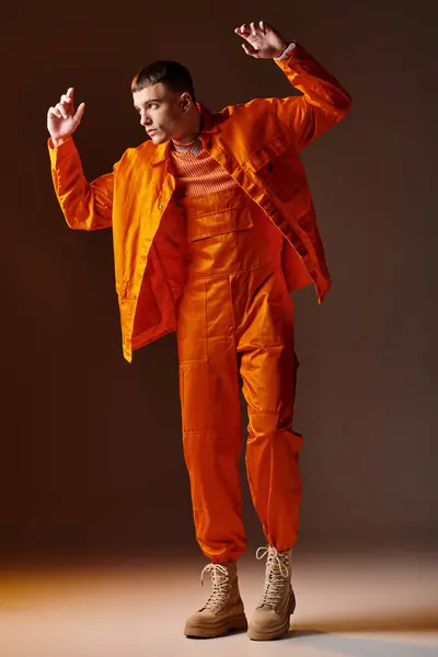 Mode pleine longueur prise de vue de l'homme élégant en combinaison orange et veste posant sur fond brun — Photo de stock
