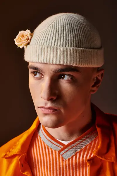 Portrait of handsome man in orange outfit wearing beige beanie with flower on brown background — Stock Photo