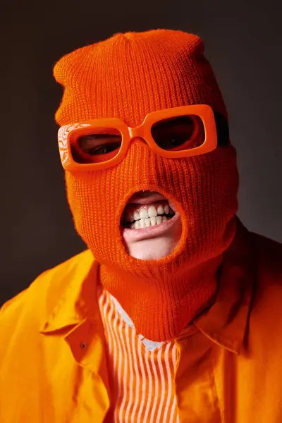 Homem irritado em roupa laranja usando máscara facial balaclava com óculos de sol laranja e mostrando dentes — Fotografia de Stock