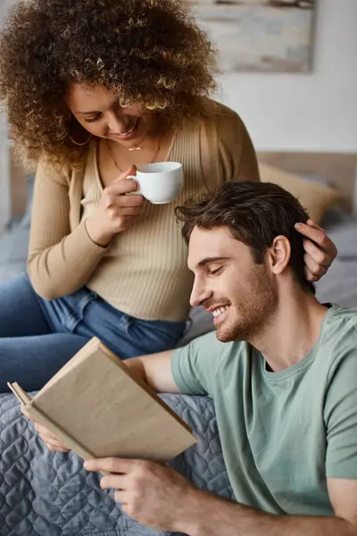 Curly young woman and brunette man engage in lively talk over coffee, book in his hands — Stock Photo