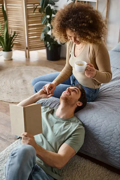 Уютная беседа за чашкой кофе и книга в постели, кудрявая женщина и брюнетка мужчина наслаждаясь компанией друг друга — стоковое фото