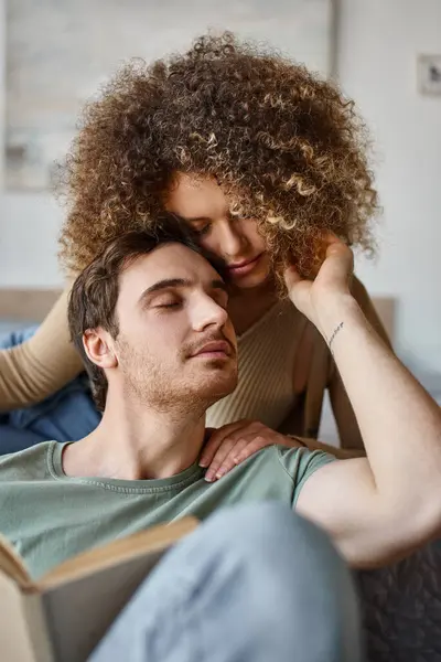 Intimate morning hug between curly young and brunette man, enjoying book together — Stock Photo
