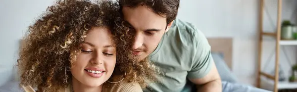 Morning cuddles and book time for curly young woman as brunette man lovingly embraces her, banner — Stock Photo
