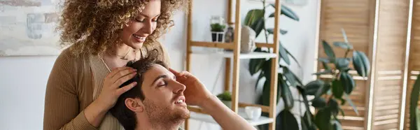 Curly young woman gently massaging boyfriends head smiling together in bedroom, banner — Stock Photo