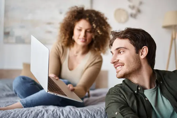Encantador jovem casal passar tempo juntos na cama, mulher mostrando tela do laptop para o homem — Fotografia de Stock