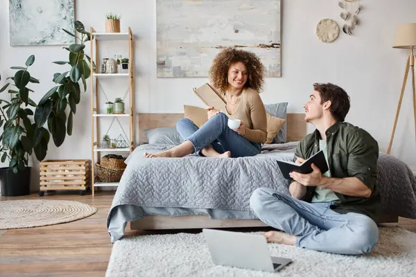 Couple working at home. Woman reading book on bed and man is working sitting on the floor — Stock Photo