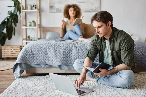 Couple working at home. Woman reading book on bed and man is working sitting on the floor — Stock Photo