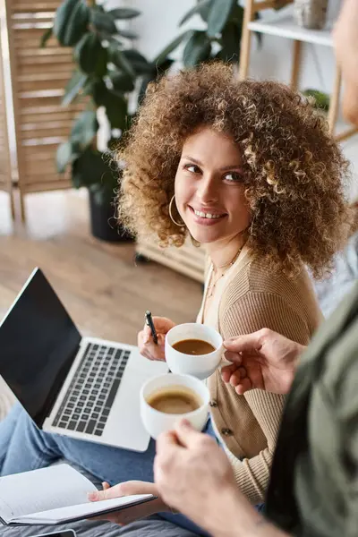 Portrait of curly woman and looking with smile at man with coffee cups sitting at bed with laptop - foto de stock