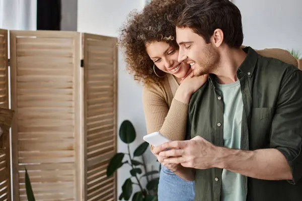 Lovely young couple spending time together at home hugging and using phone with smile — Stock Photo