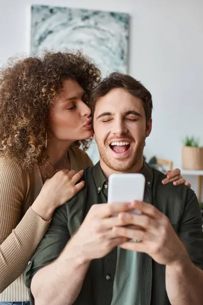 Lovely young couple embracing spending time together at home hugging and using phone — Stock Photo