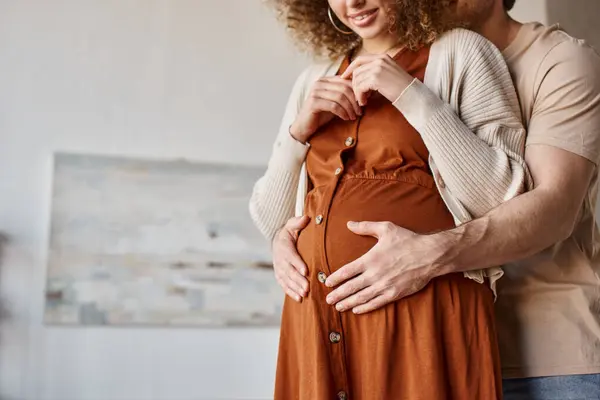 Vista cortada do homem abraçando sua esposa grávida por trás de pé em casa esperando pelo bebê — Fotografia de Stock