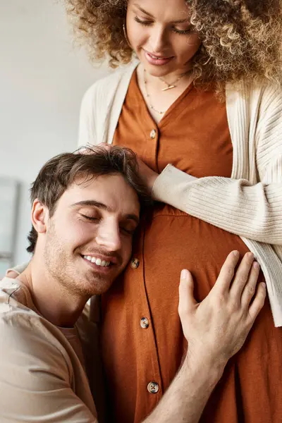 Эмоциональный момент счастливого мужчины, слушающего, как малыш обнимает животик жены, трогает её живот — стоковое фото