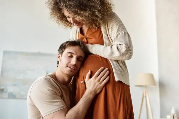 Красивый улыбающийся счастливый мужчина слушает, как малыш обнимает животик жены, трогает её живот — стоковое фото