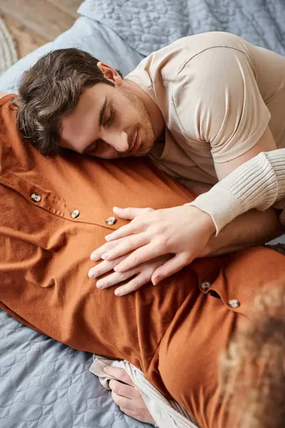 Обрізаний вид вагітної жінки з чоловіком у спальні, лежачи в ліжку, чоловік торкається живота — стокове фото