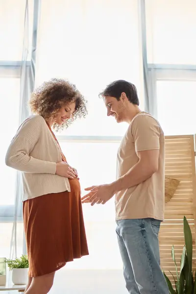 Пара ожидающих ребенка, проводящих время вместе дома, мужчина трогает беременную жену живот — стоковое фото