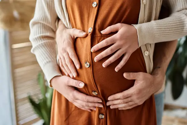 Ожидая детскую пару, обрезанный вид мужчины, обнимающего свою беременную жену сзади — стоковое фото