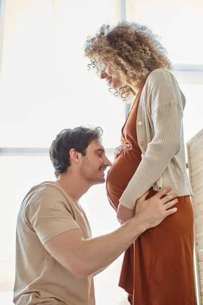 Vista lateral de hombre feliz sonriente esperando bebé besos vientre de la esposa con los ojos cerrados - foto de stock