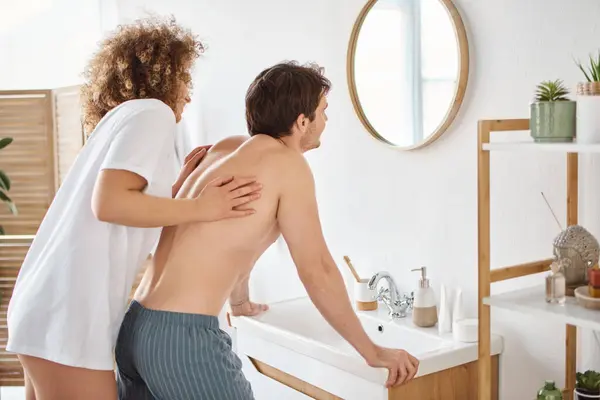 Back view of curly young woman and brunette man in bathroom looking in mirror, enjoying the morning — Stock Photo