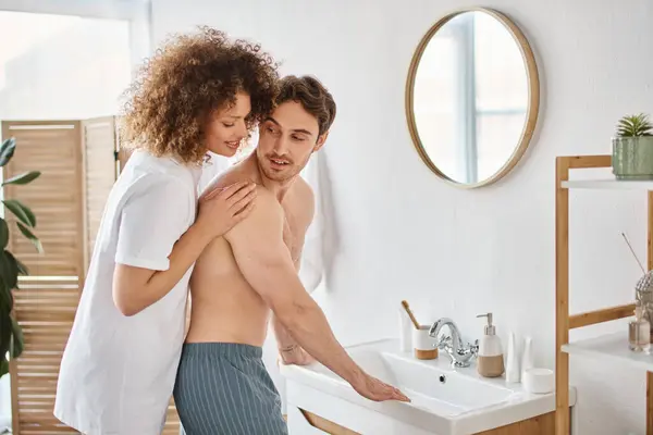 Side view of curly young woman and brunette man in bathroom hugging in love and smiling — Stock Photo