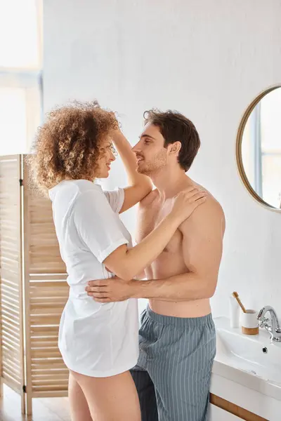 Curly young woman and brunette man in bathroom hugging in love and smiling looking at each other — Stock Photo