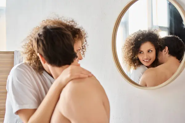 Vue latérale de la jeune femme bouclée et brune homme dans la salle de bain étreignant dans l'amour et souriant — Photo de stock