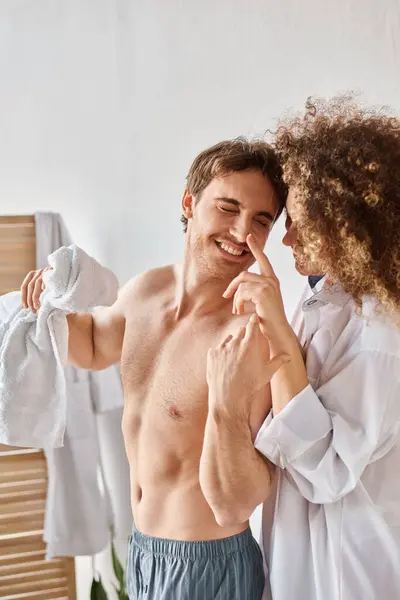 Happy couple in love in bathroom, woman applying cream to her man in bathroom and smiling - foto de stock