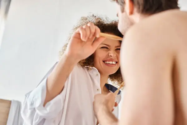 Joven pareja feliz riendo y divirtiéndose mientras se cepillan los dientes juntos en la mañana - foto de stock