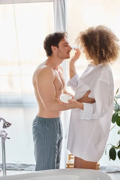 Woman applying cream to her man nose in bathroom and smiling. Couple bonding in the morning — Stock Photo