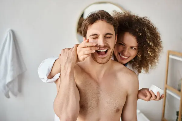 Couple cuddling and bonding. Woman applying cream to her man in bathroom and laughing together — Stock Photo