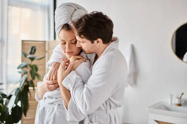 Portrait of happy man and woman in love in bathrobes in the bathroom, hugging each other — Stock Photo