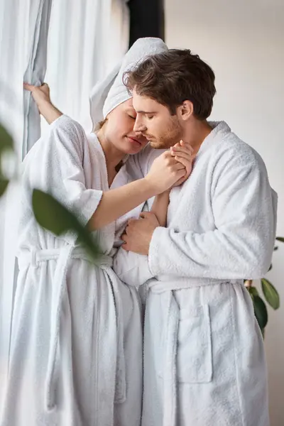 Couple in love wearing bathrobes hugging each other and having loving moment near window — Stock Photo