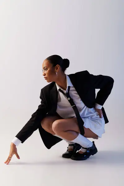 Jeune femme afro-américaine en costume et cravate à genoux dans un cadre de studio — Photo de stock