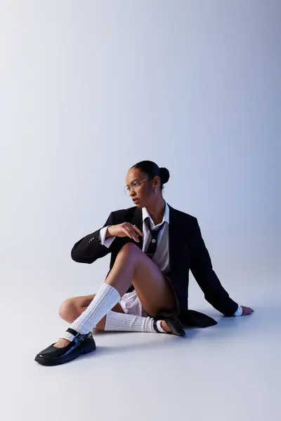 Young African American woman sitting on ground in suit and tie, white studio — Stock Photo