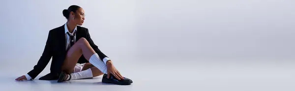 A young African American woman in a stylish suit sits confidently on the floor in a studio setting, banner — Stock Photo