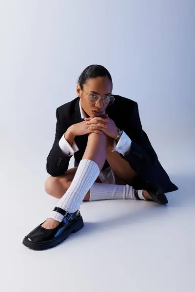 Joven mujer afroamericana sentada con las piernas cruzadas en el suelo en una pose pacífica en el estudio - foto de stock
