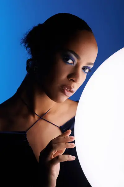 Young African American woman delicately cradles a white ball in her hands, in a studio setting. — Stock Photo