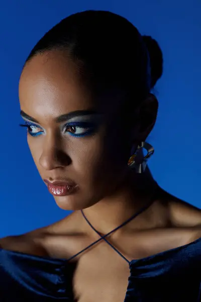 Una joven afroamericana está de pie con un vestido negro, sus penetrantes ojos azules cautivando al espectador. - foto de stock