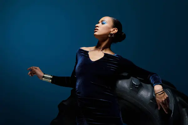 Молодая афроамериканка в синем платье изящно позирует возле шины — стоковое фото