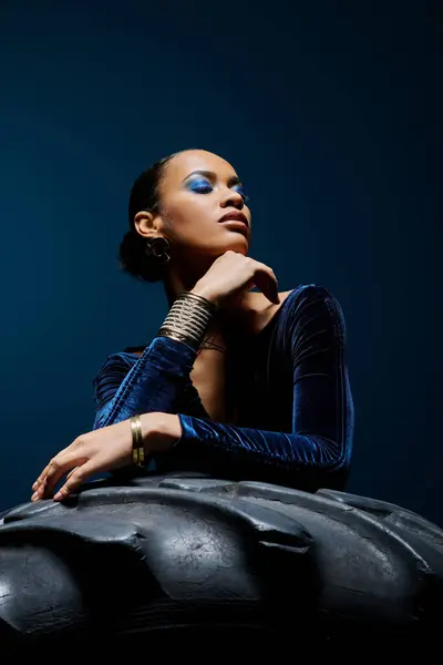 A young African American woman confidently sits atop a worn tire in a studio setting. — Stock Photo