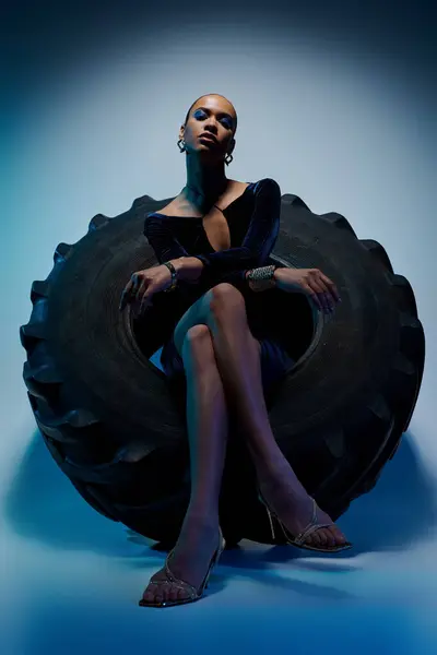 A young African American woman confidently sits atop a colossal tire in a creative studio setting. — Stock Photo