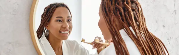 Африканська американка з афро косами чистить зуби в сучасній ванній кімнаті, зосереджуючись на її красі та гігієні. — стокове фото