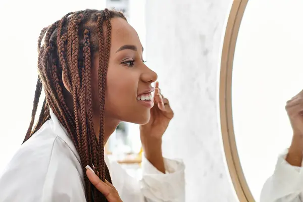 Африканська американка з афро косами, використовуючи бавовняну майданчик у сучасній ванній кімнаті, зосереджена на її повсякденній рутині краси. — стокове фото