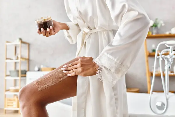 Афроамериканка в халате, наносила кофейный скраб в современной ванной. — стоковое фото