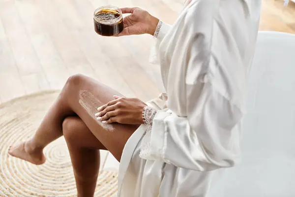 Eine Afroamerikanerin sitzt auf einer Badewanne und peelt ihr Bein mit Peeling — Stockfoto