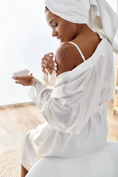 Femme afro-américaine en robe blanche appréciant la crème sur son corps — Photo de stock