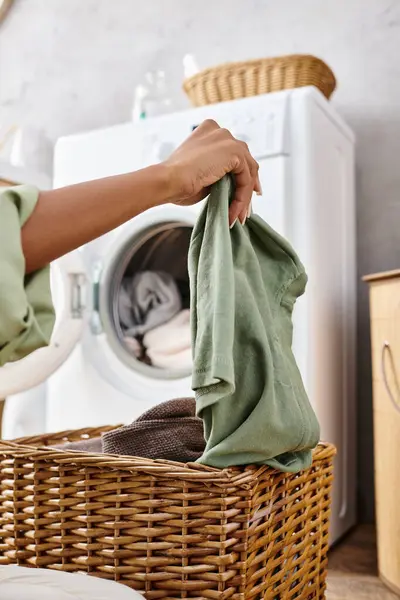 Africano mulher americana com tranças afro segurando um saco de roupa na frente de uma máquina de lavar roupa em um banheiro. — Fotografia de Stock
