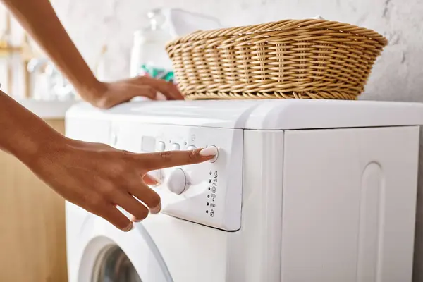 Mujer afroamericana con trenzas afro pulsando el botón en la lavadora haciendo la colada en el baño. - foto de stock