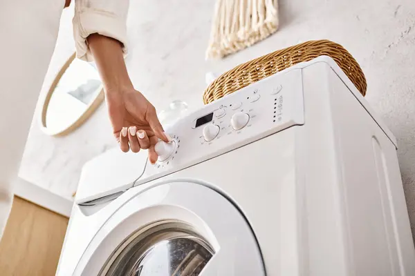 Une Afro-Américaine appuyant sur un bouton sur une machine à laver dans une salle de bain, faisant la lessive. — Photo de stock